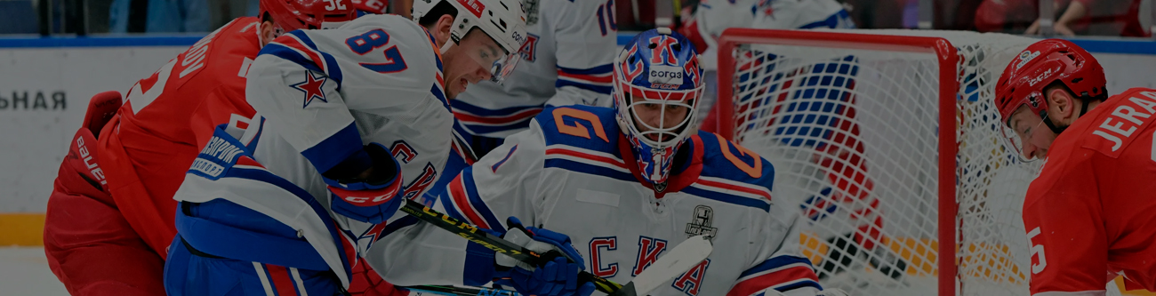 Хоккейный матч: игроки в бело-синих и красных формах борются около ворот. Вратарь в бело-синей форме готовится отразить шайбу. Напряжённая атмосфера в разгаре игры