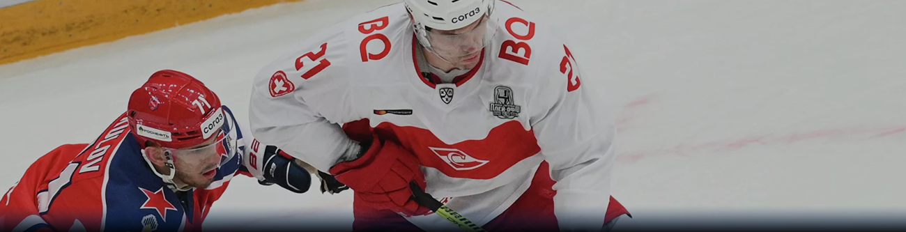 Хоккеист в белой форме с номером 21 борется за шайбу с соперником в красной форме на льду. Игроки сосредоточены, ледовая площадка видна частично